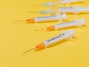 Pfizer and AstraZeneca Vaccines Yellow Background Syringes